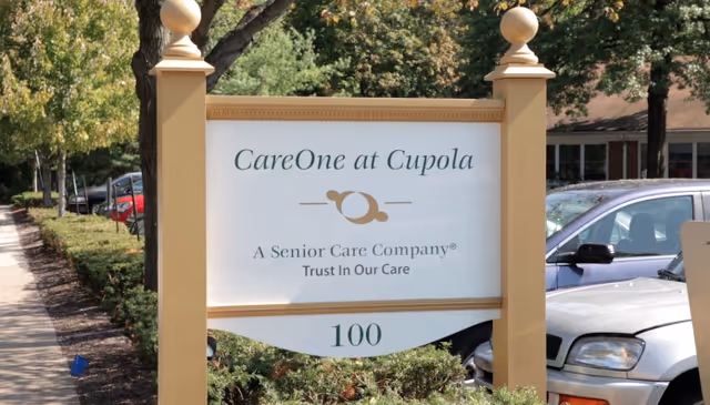 Entrance sign reads CareOne at Cupola, with parking lot and trees nearby.