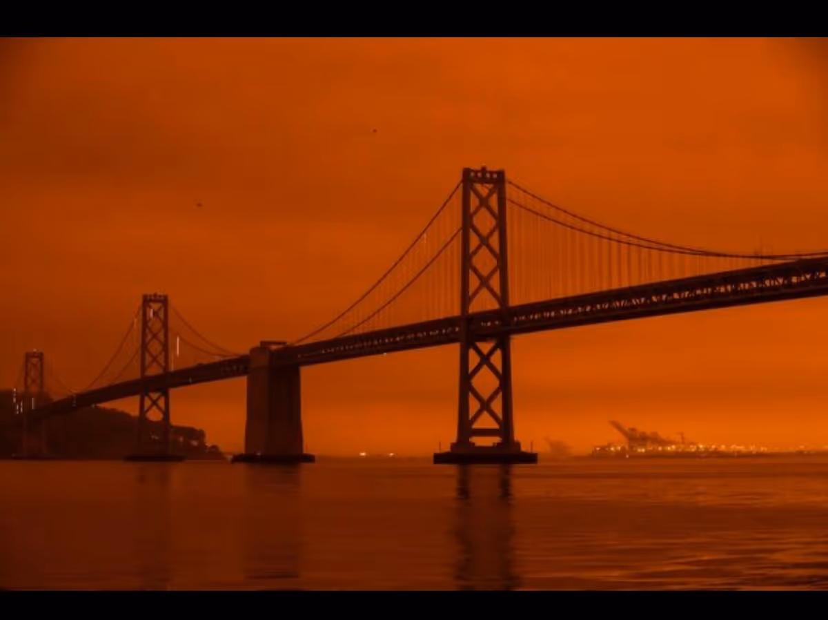 Orange sunset over a large suspension bridge spanning calm water.