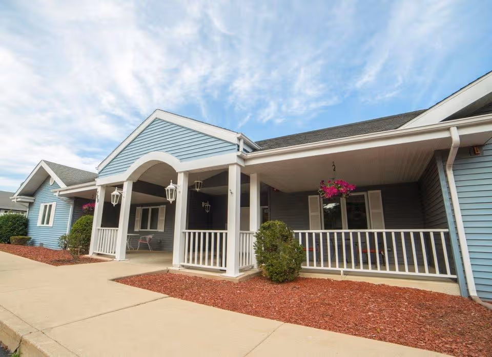 Harbor House Memory Care exterior with a covered porch, white railings, and hanging baskets.