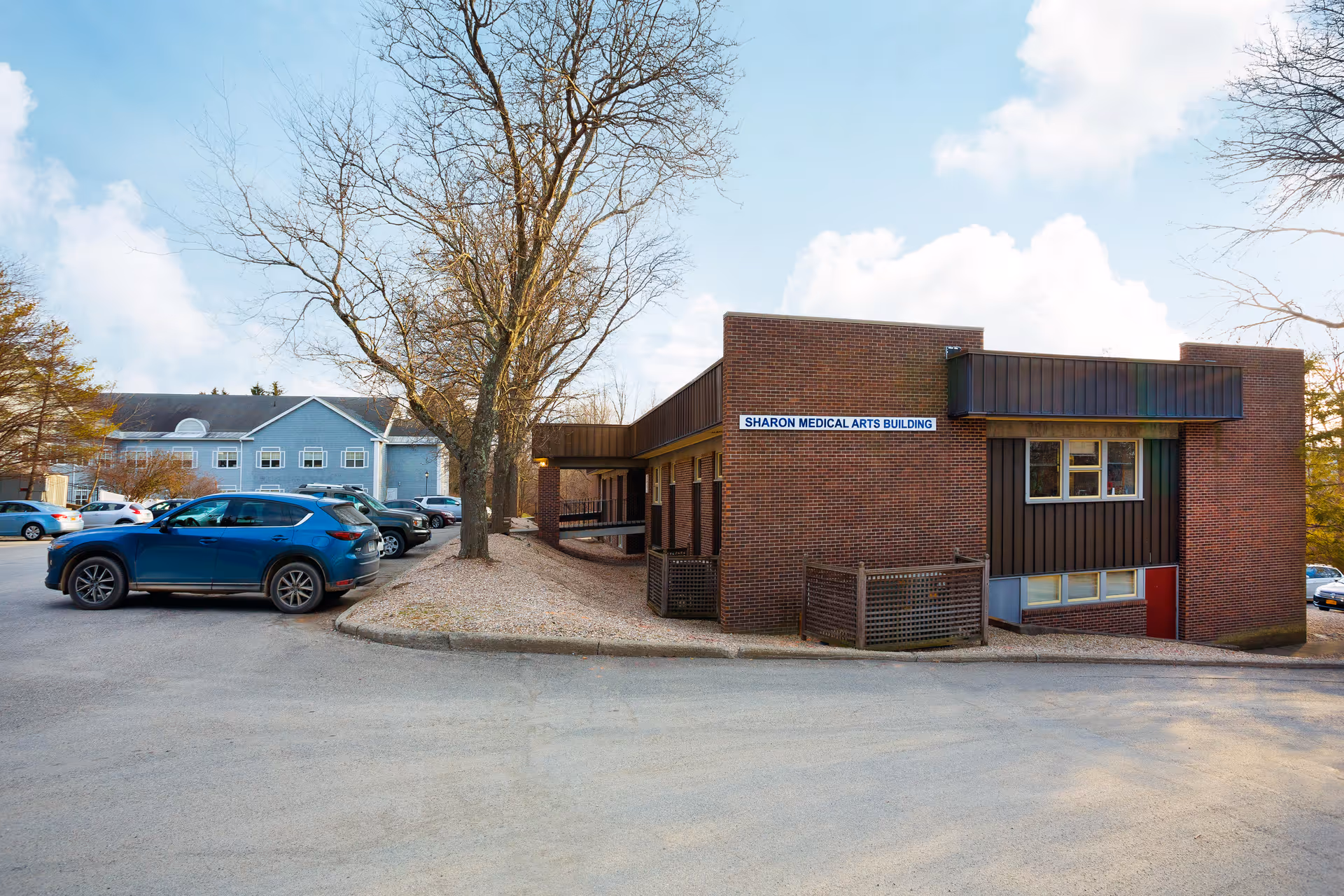 Exterior view of Sharon Medical Arts Building, a brick facility with parked cars and trees.