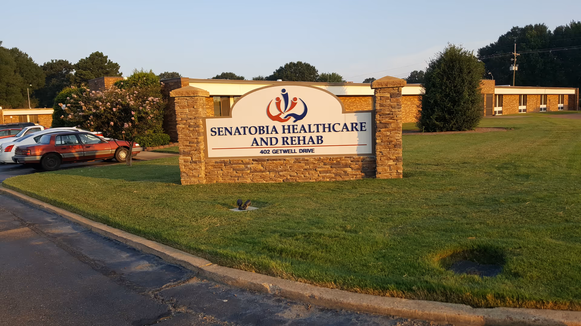 Exterior view of Senatobia Healthcare and Rehab sign with stone pillars and nearby parking.