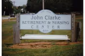 Outdoor view of John Clarke Retirement and Nursing Center sign with a bench.