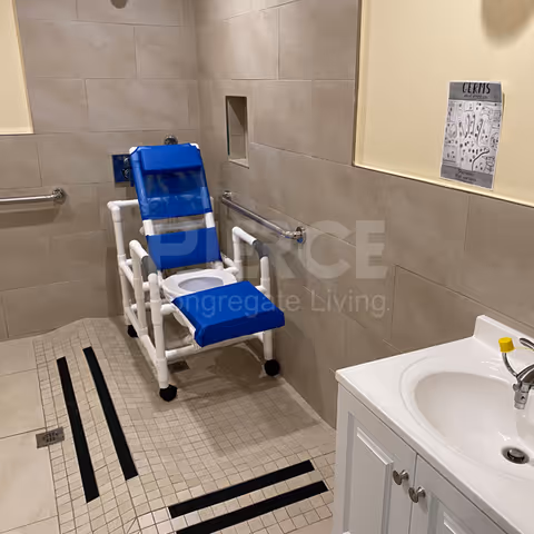 Blue padded shower chair with armrests in a tiled senior living bathroom.