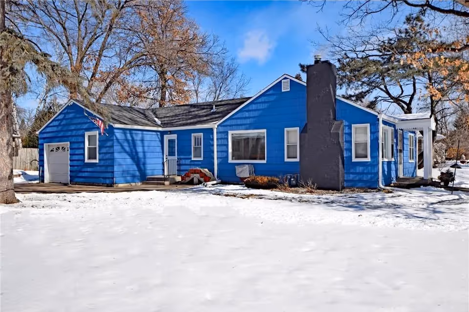 Bright blue single-story building with a chimney, snow-covered ground, and bare trees.