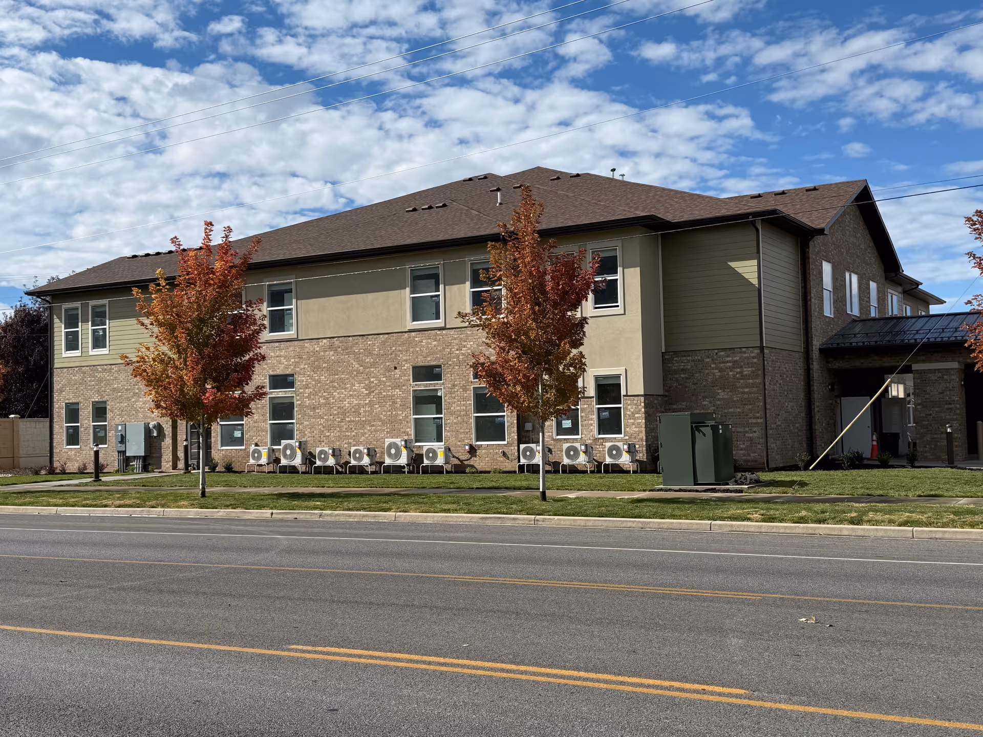 Maple Landing Assisted Living facility with beige brick facade, trees, and row of outdoor HVAC units.