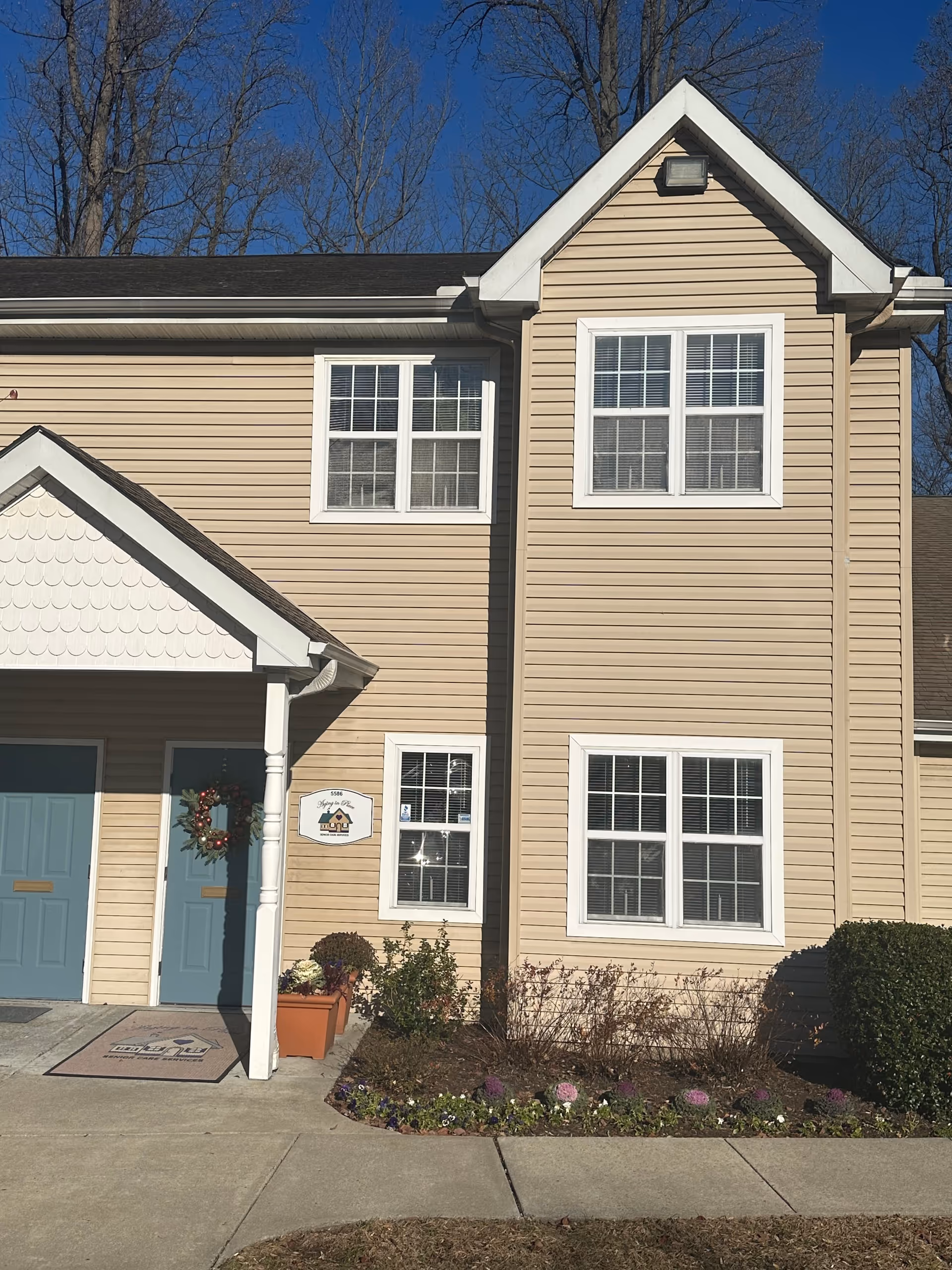 Two-story beige senior care building with blue doors and a wreath at the entrance.