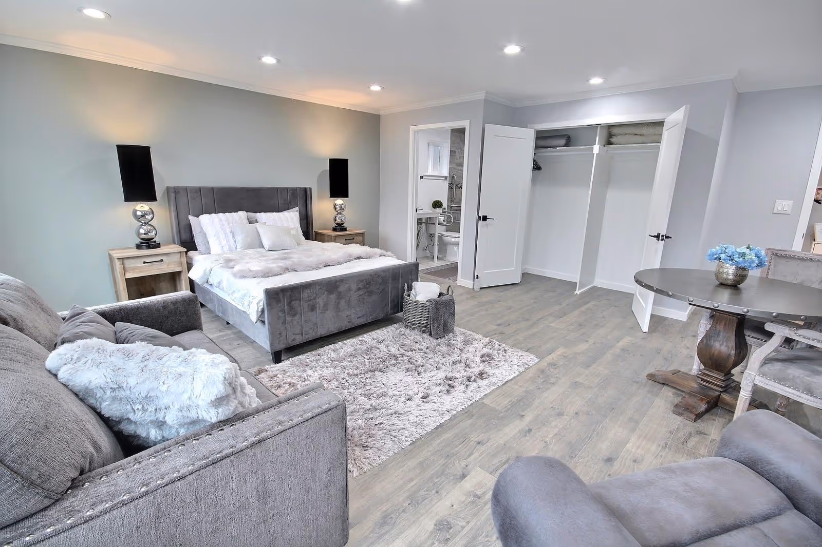 Cozy modern bedroom suite with a bed, seating area, open closet, and round table.