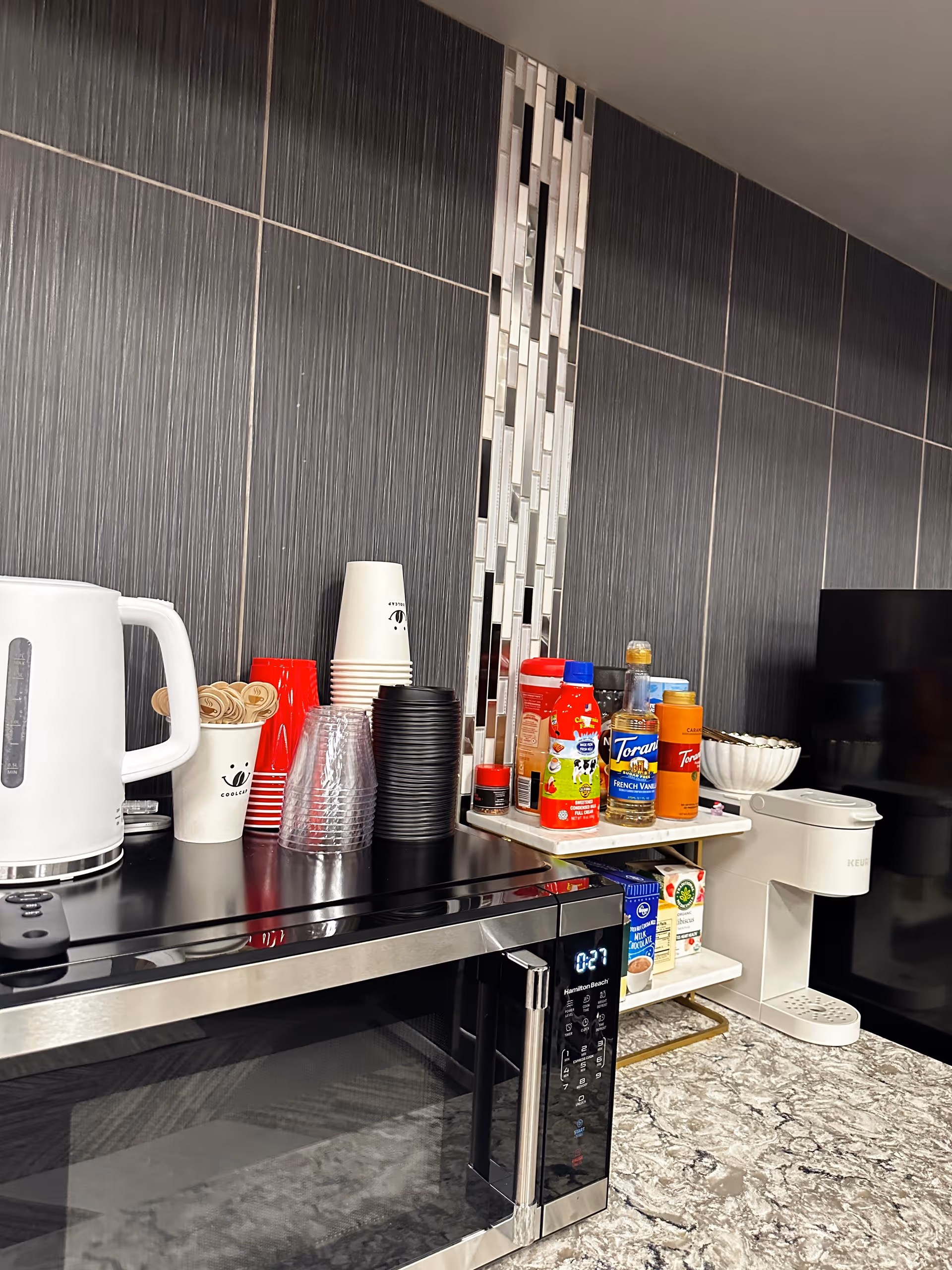 Modern senior living kitchenette with kettle, cups, microwave, and beverage station.