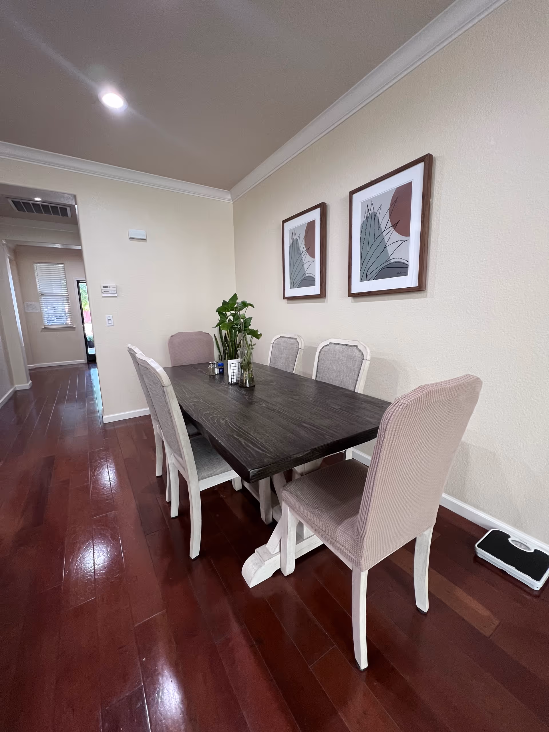 A long dark dining table with beige upholstered chairs in a bright dining room.