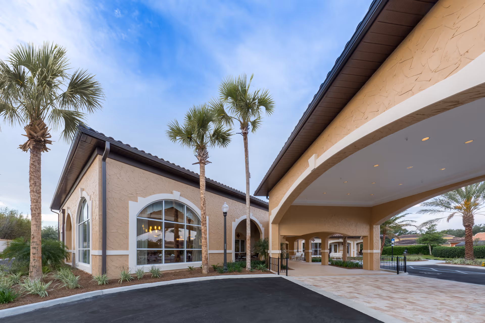 Watercrest Spanish Springs senior living exterior with arches, palm trees, and a covered entrance