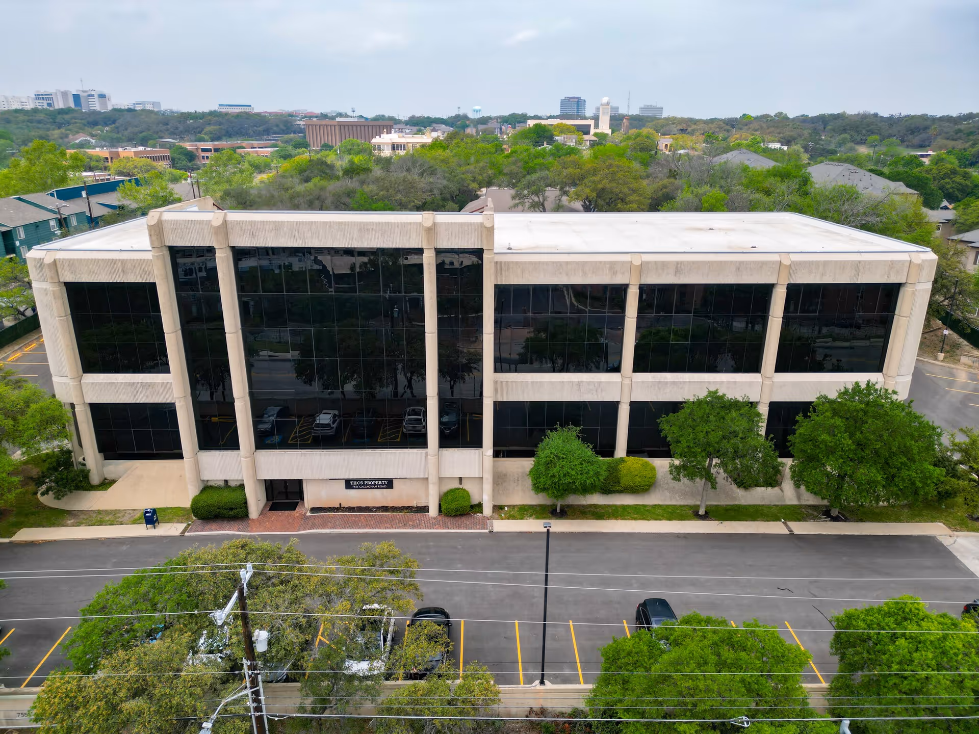 Two-story glass-front building with a parking lot and surrounding trees.