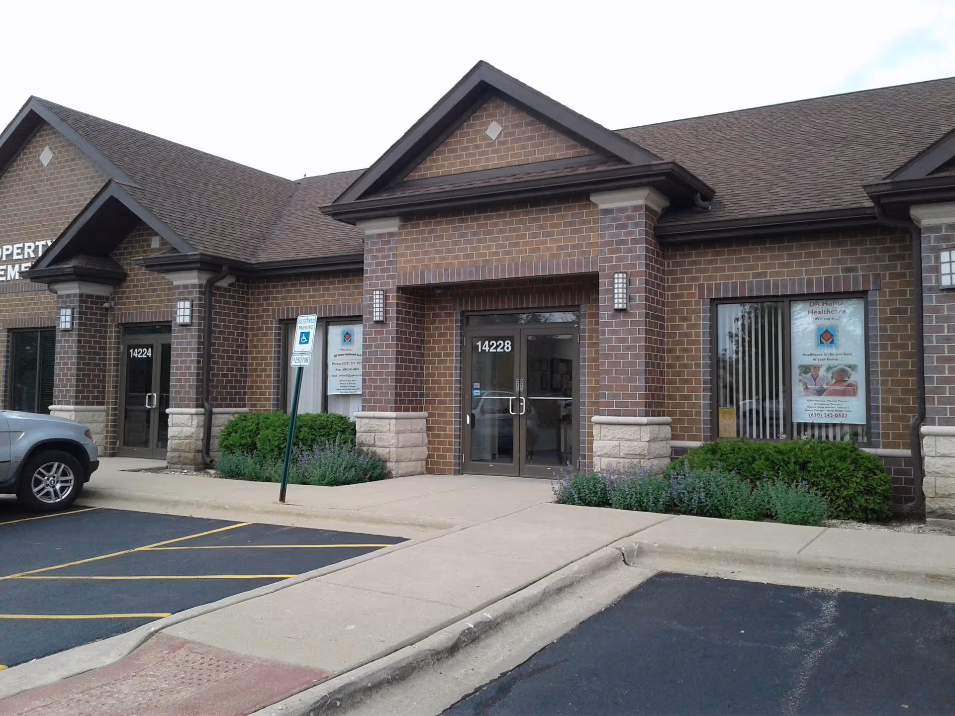 Brick storefront with glass doors and a parking lot in front of a senior care facility.