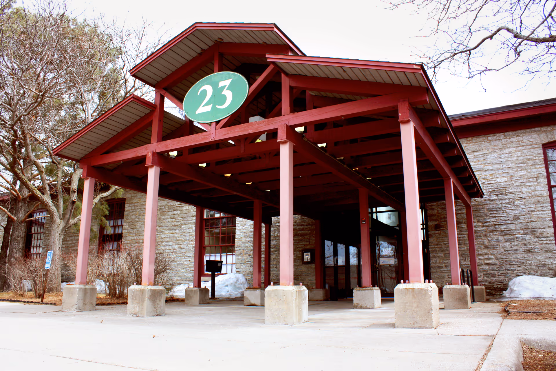Red wooden entrance canopy with a green 23 sign over a stone-front building.