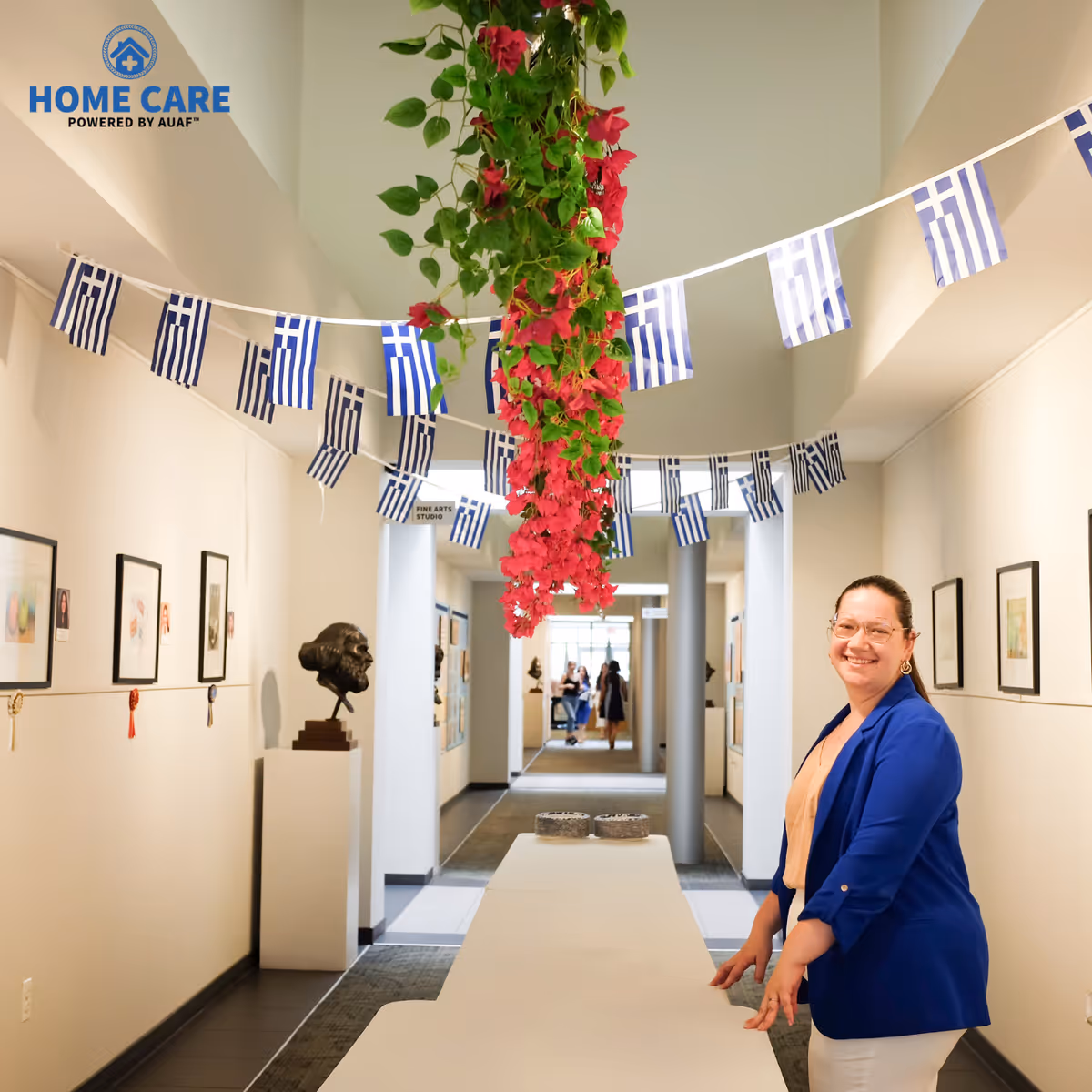 Smiling staff member in a well-lit hallway with flags and hanging flowers.