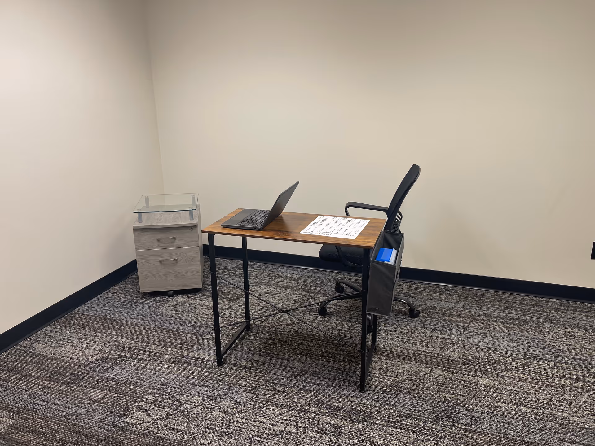 Empty office workspace with a desk, laptop, chair, and rolling file cabinet.