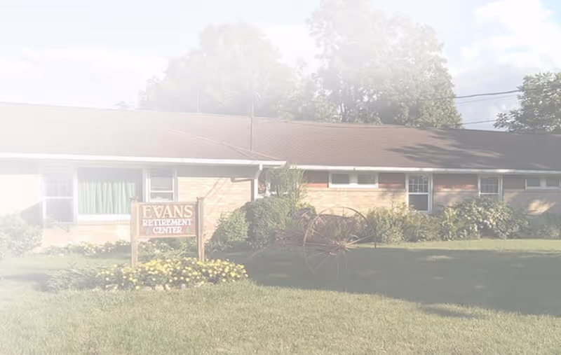 Front exterior of Evans Retirement Center with sign, shrubs, and a wagon wheel.