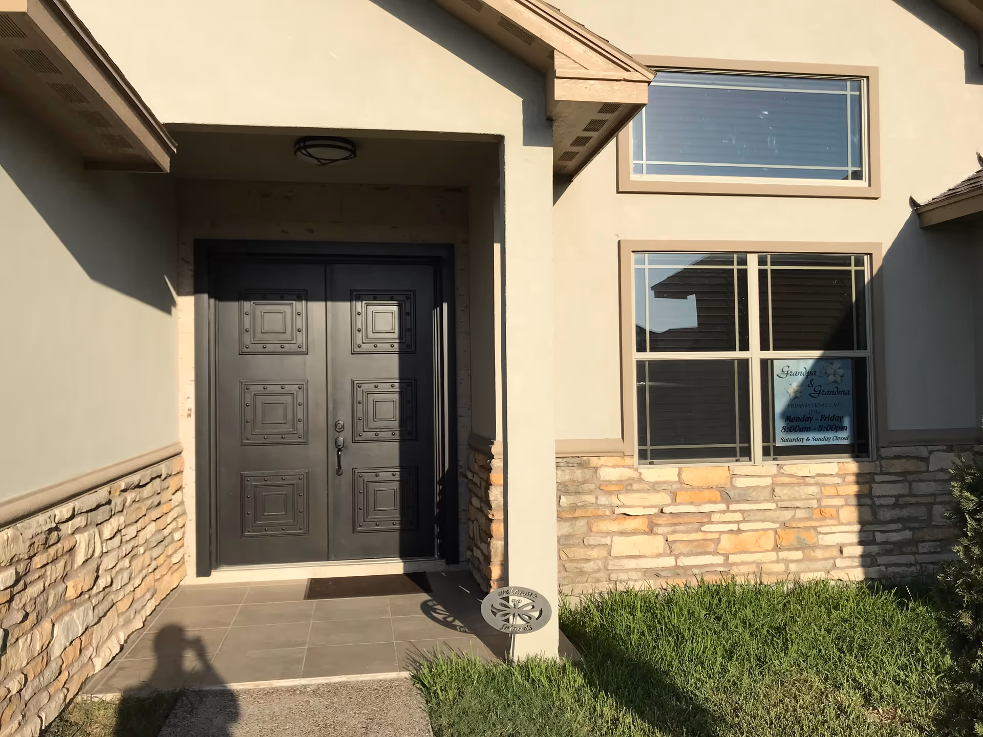 Front entrance of a beige building with a large black double door and stone accents.