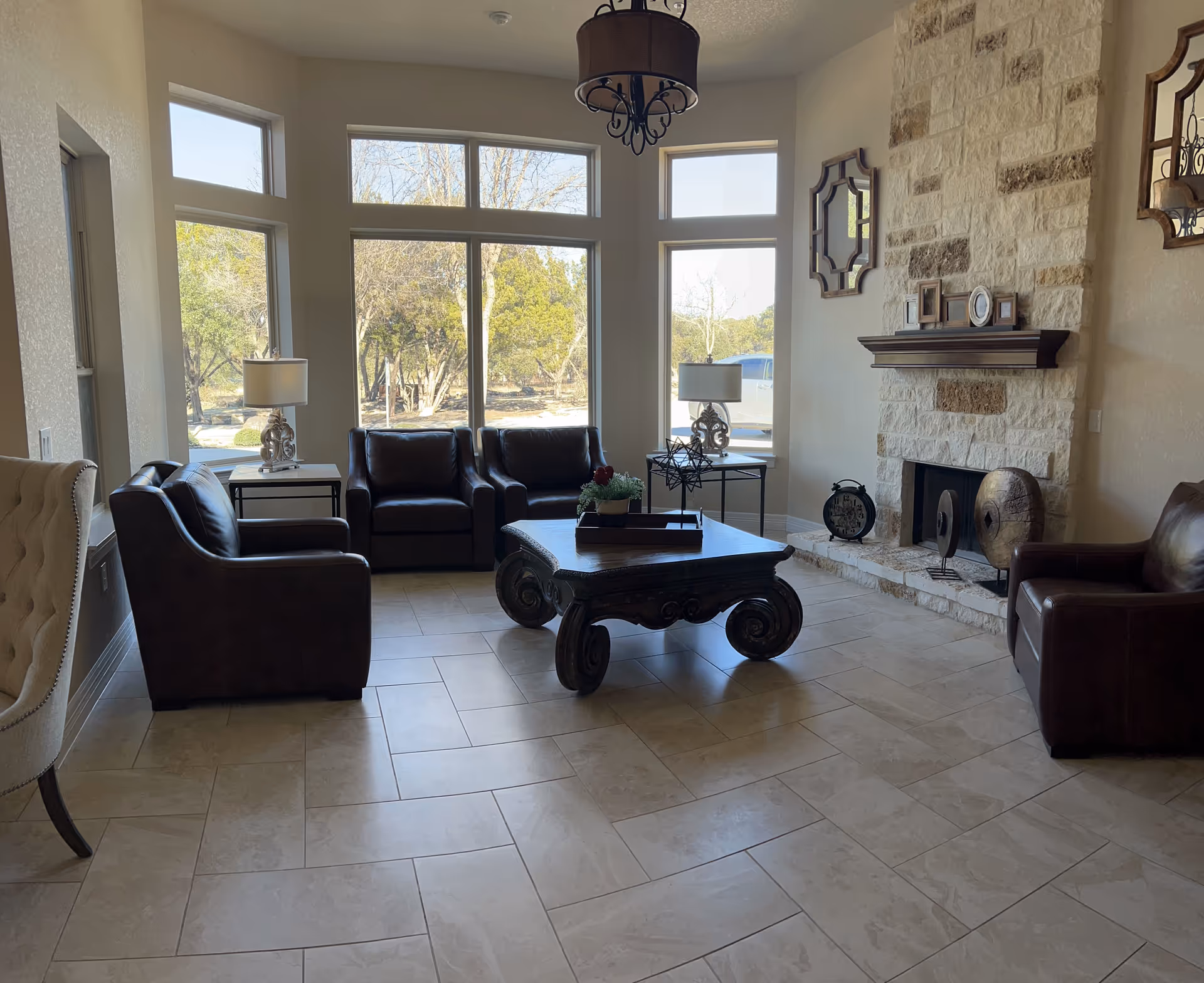 Bright seating area with leather chairs, a stone fireplace, coffee table, and large windows