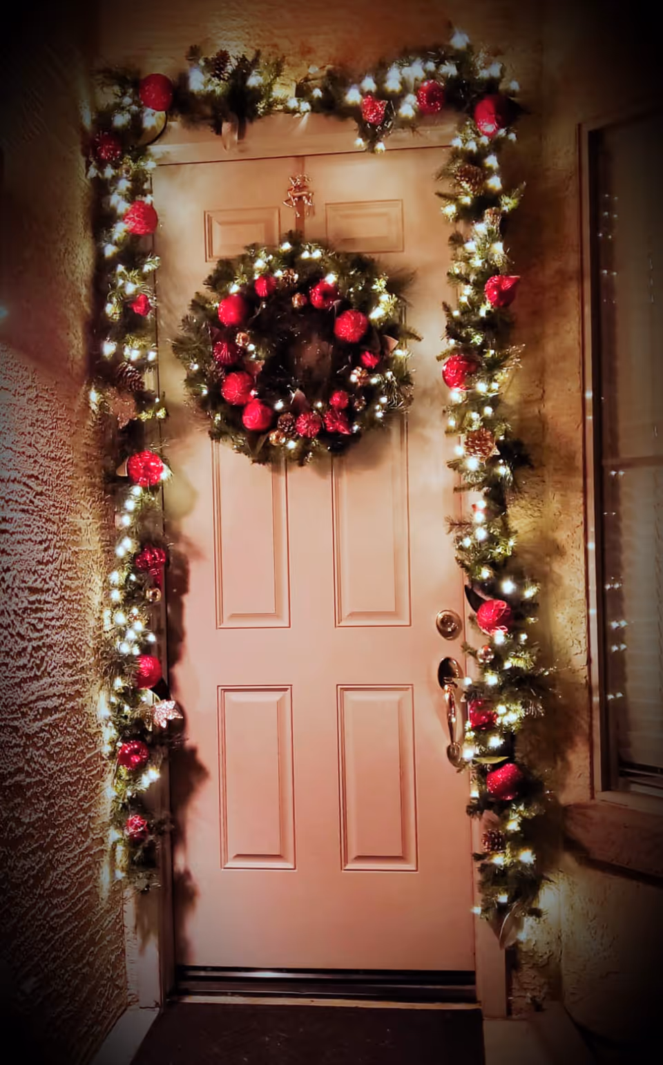 Decorated front door with garland and wreath lit by warm holiday lights.