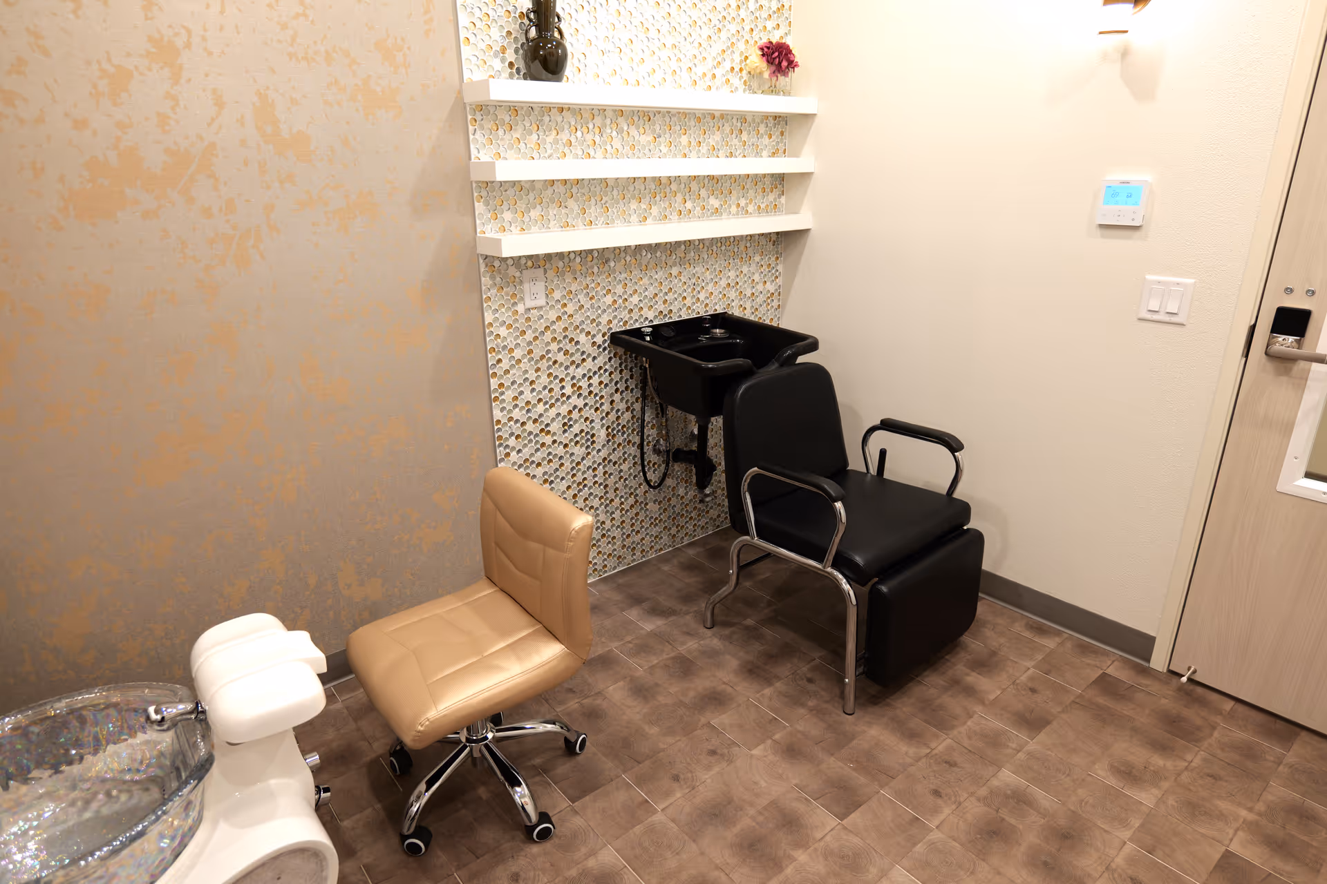 Salon area with a beige styling chair, black reclining chair, and washing basin.