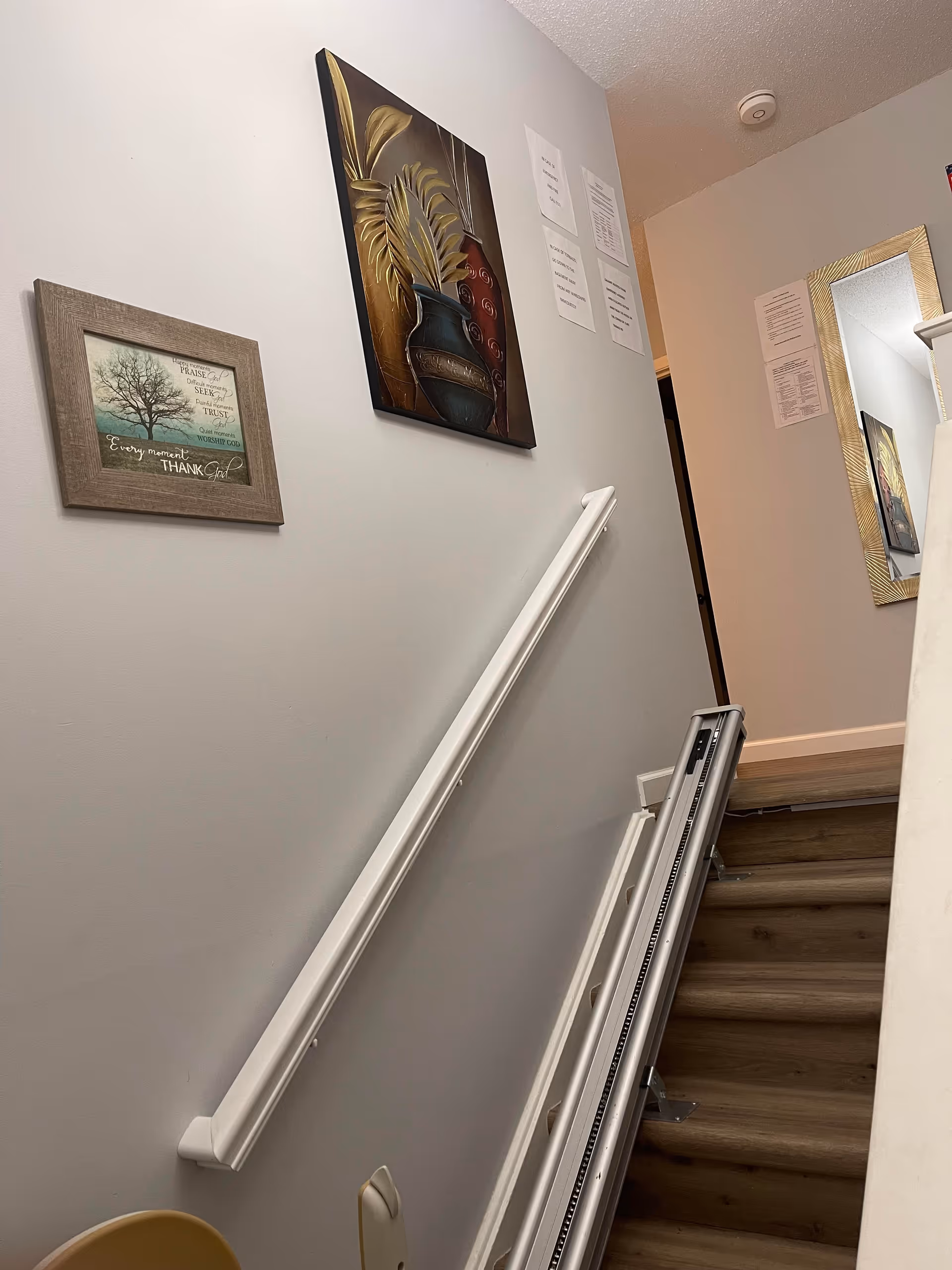 Indoor stairwell with handrails, wall art, and a stairlift along a residential hallway.