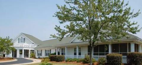 A single-story senior living building with a curved driveway and landscaped front yard.