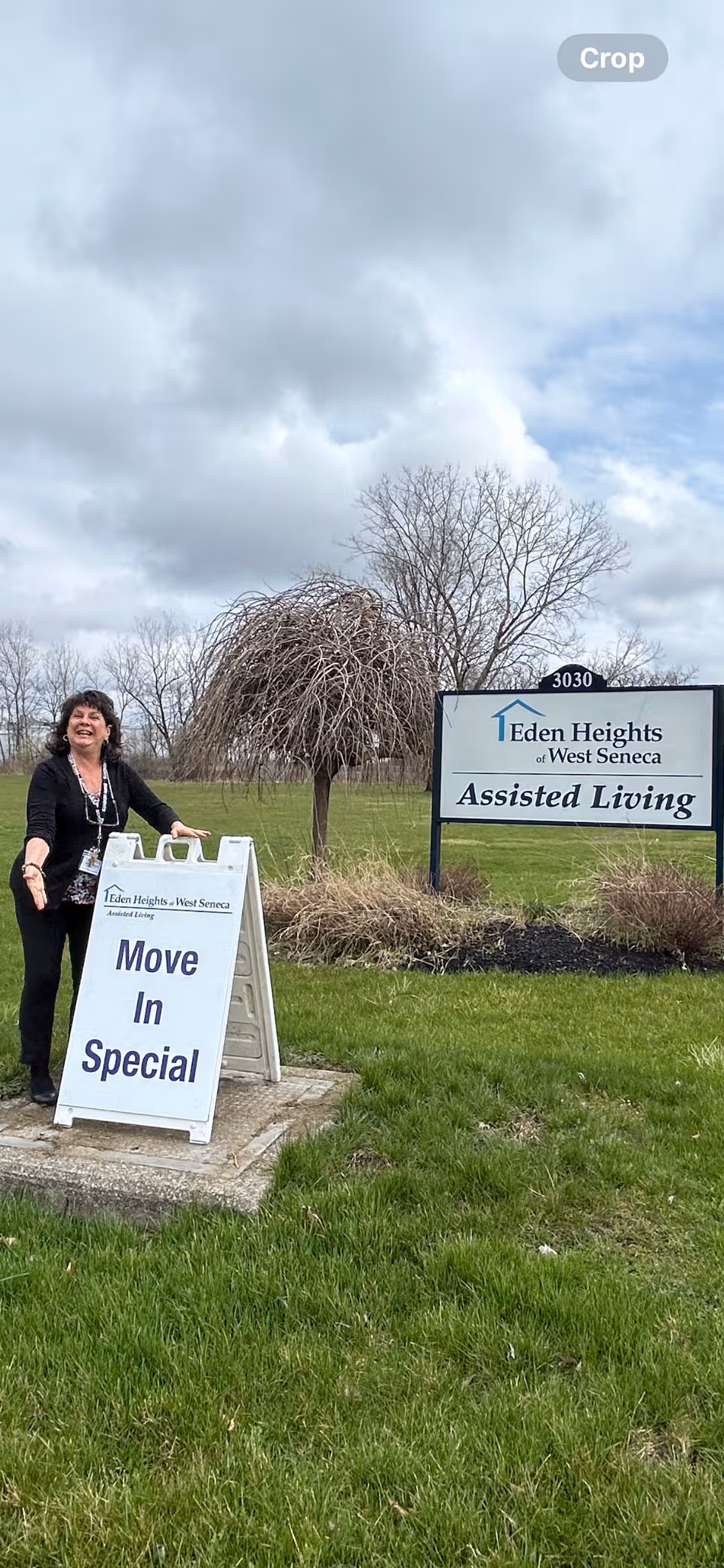 A woman stands beside a Move In Special sign outside Eden Heights Assisted Living.