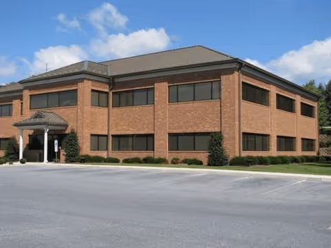 Brick two-story building with a covered entrance, surrounding shrubs, and a parking lot.
