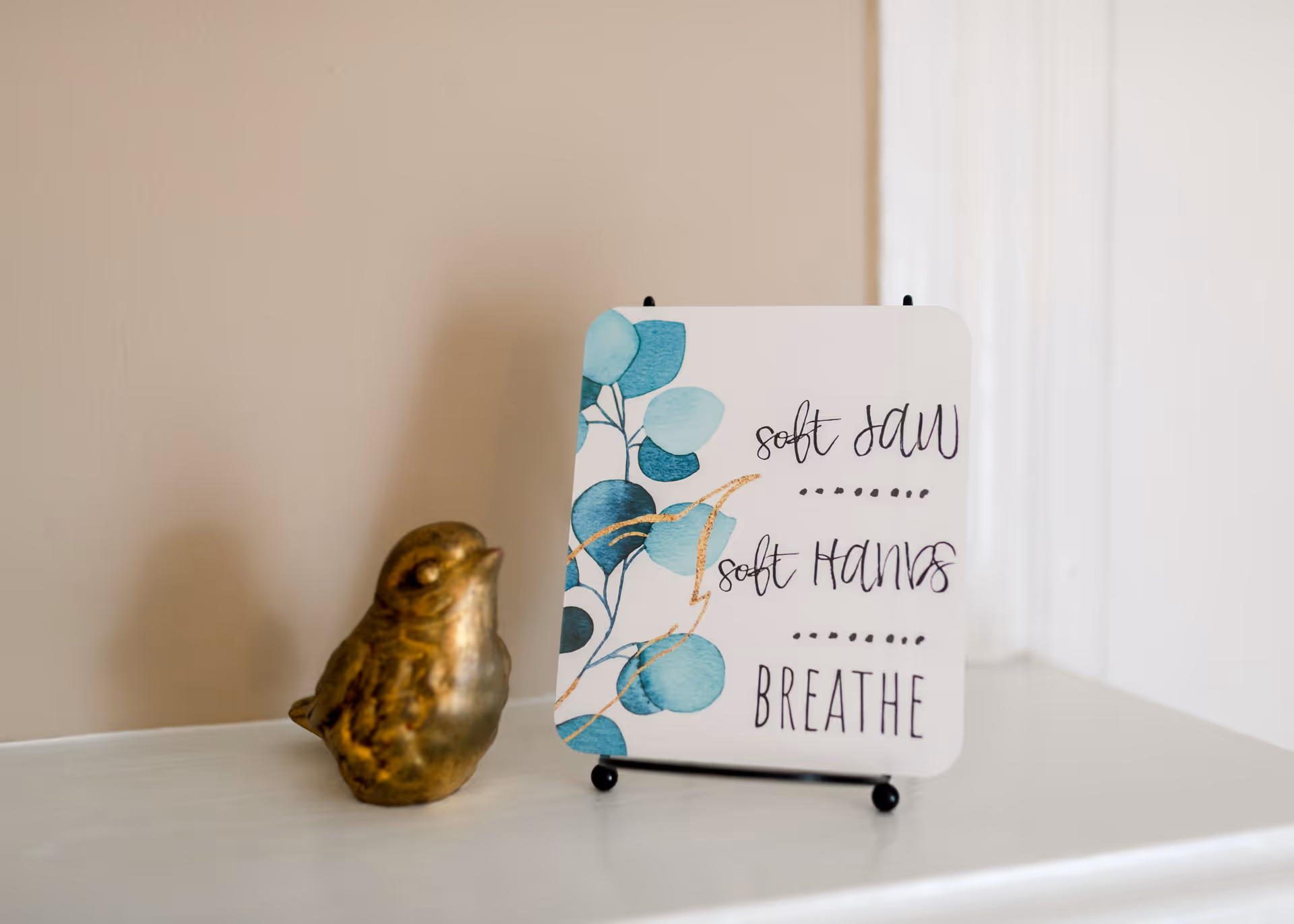 Decorative sign with blue leaves beside a bronze bird on a shelf.
