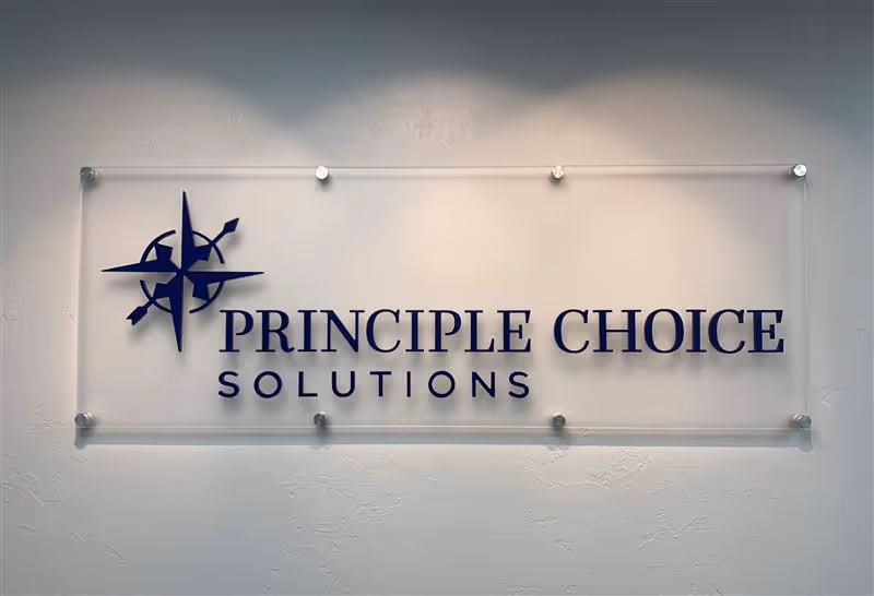 A frosted acrylic sign reading PRINCIPLE CHOICE SOLUTIONS mounted on a wall.