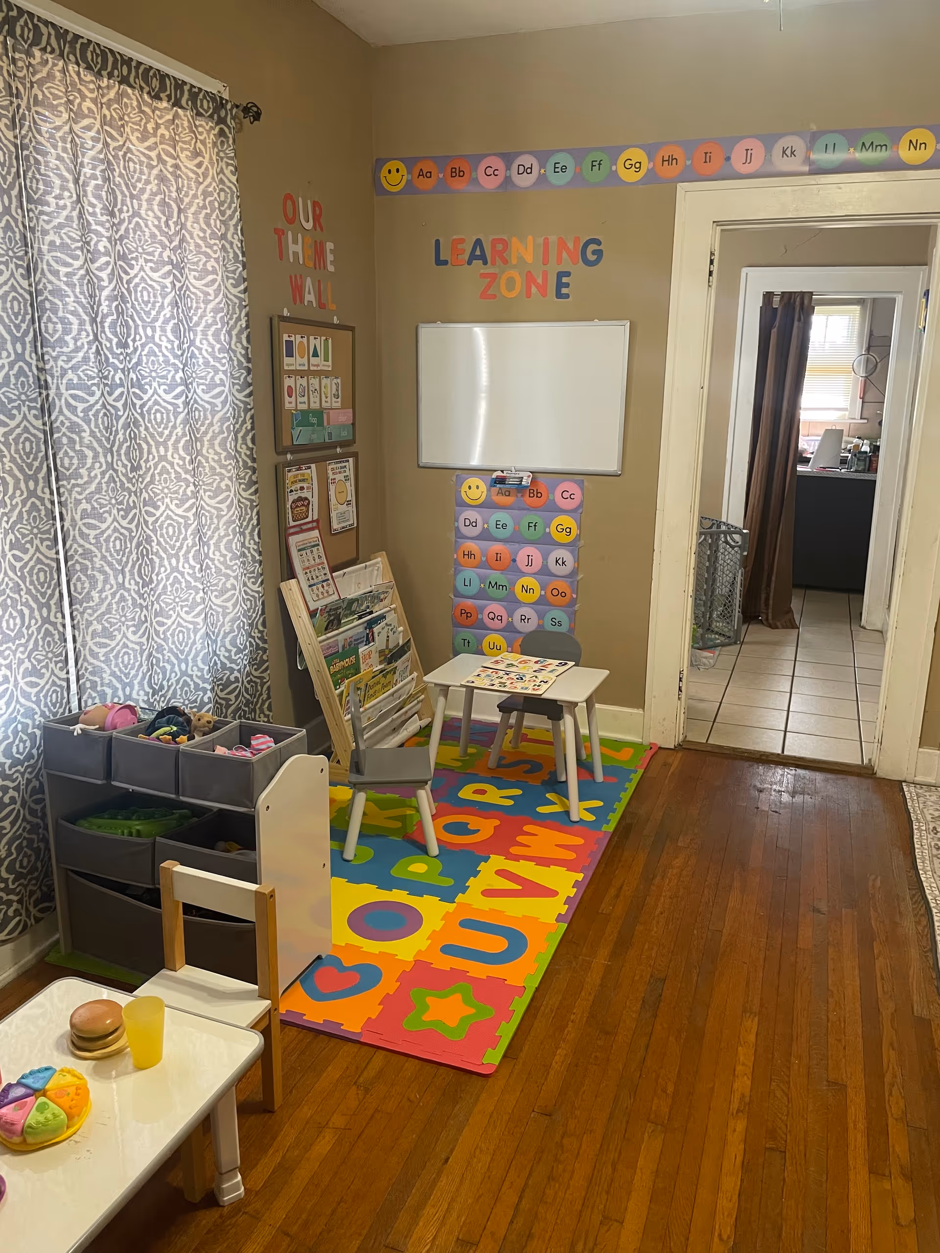 Colorful learning corner with alphabet rug, small table, toy shelves in a senior living facility interior.