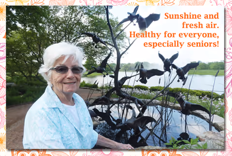 An elderly woman in a light blue jacket beside a metal bird sculpture by a pond