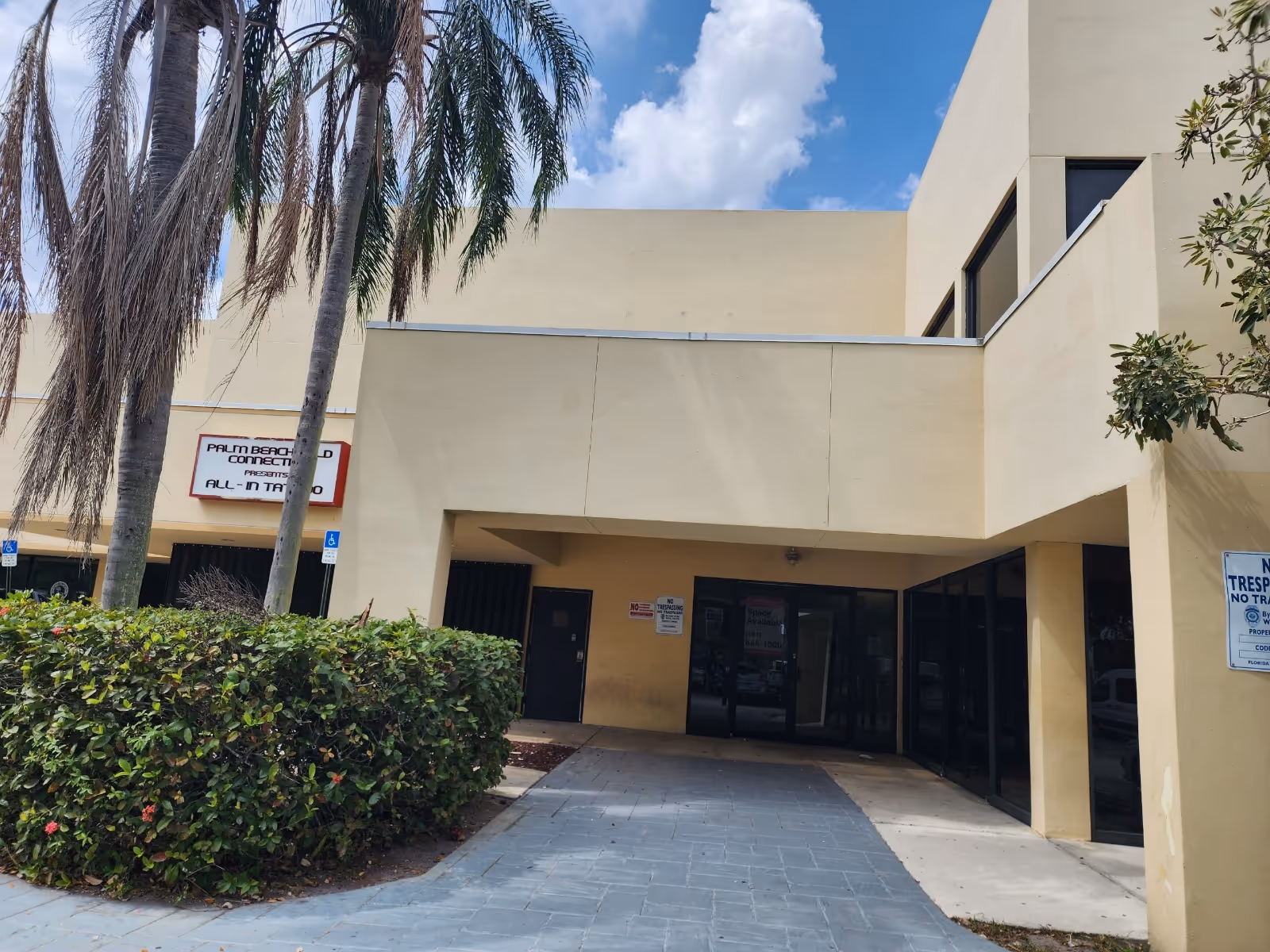 Exterior view of a beige building entrance with palm trees and glass doors