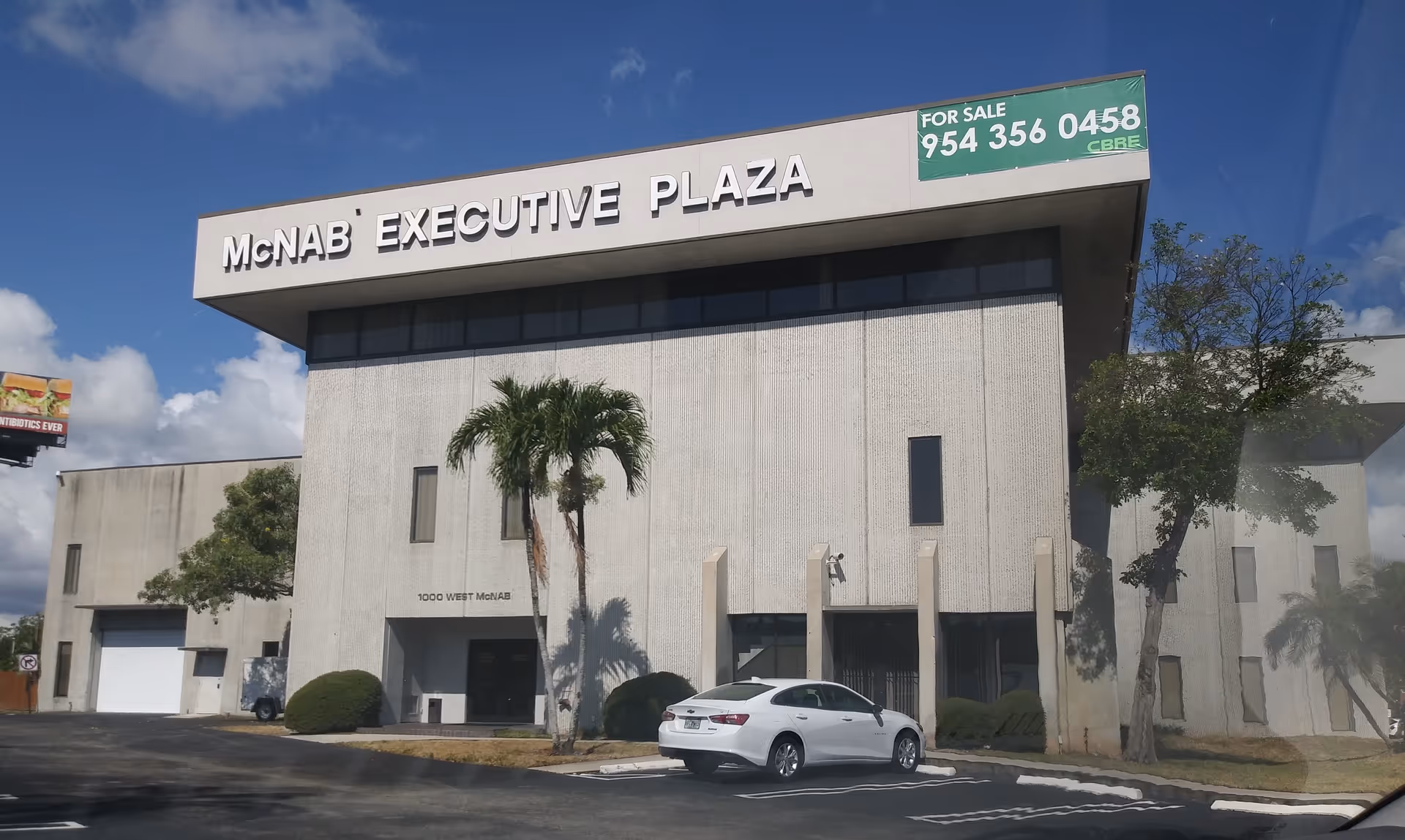 Front view of a large office building labeled McNAB Executive Plaza with a white car.