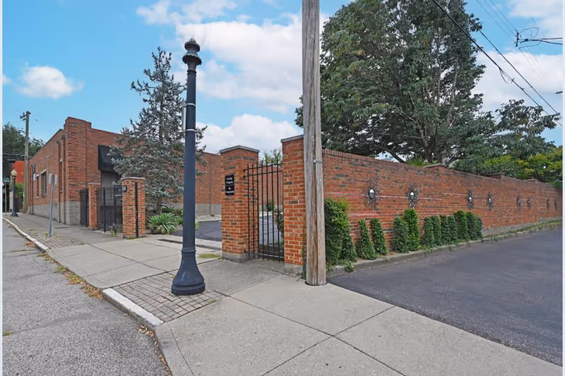 A brick-walled facility with a gated entrance along a sidewalk and street.