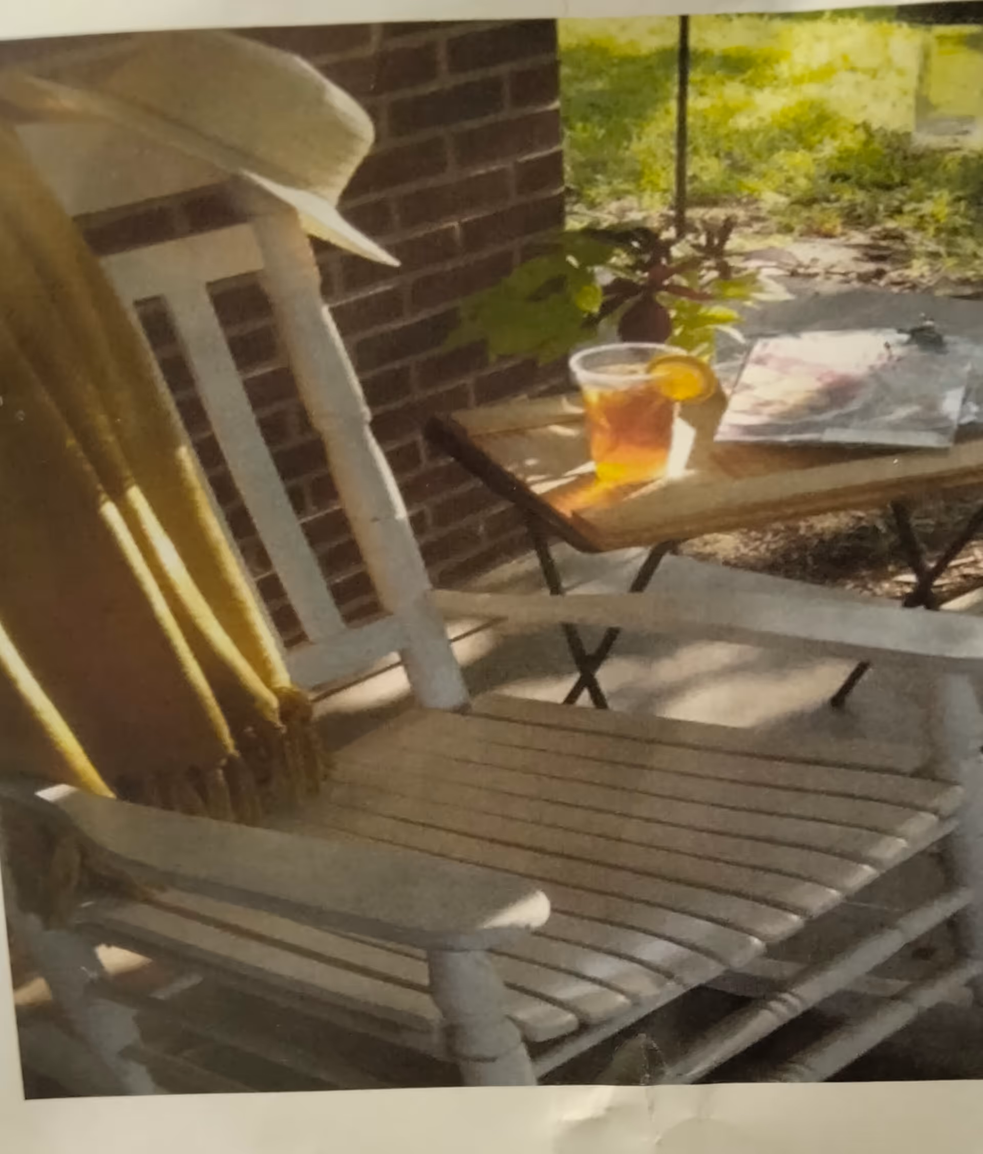 Outdoor porch scene with white wooden chair, small table, iced drink, plant, and sunlight.