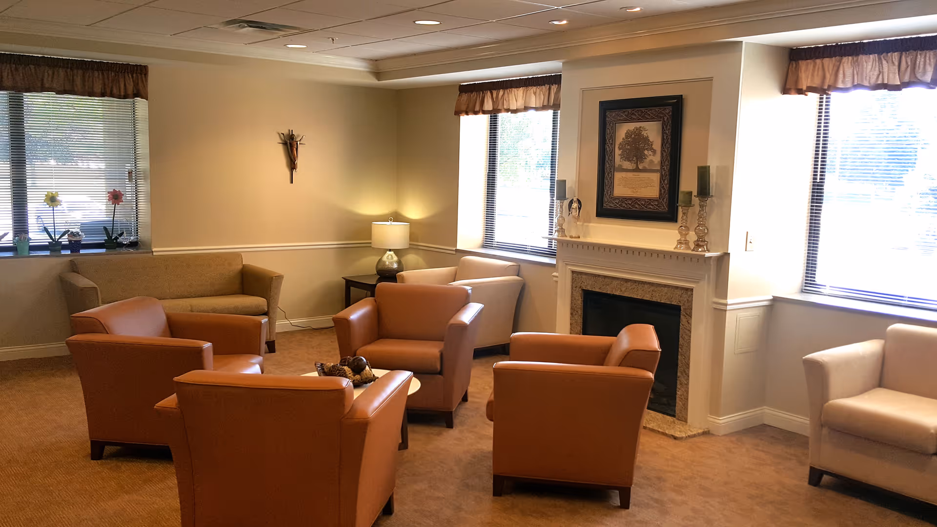 Cozy senior living lounge with orange chairs around a coffee table by a fireplace.