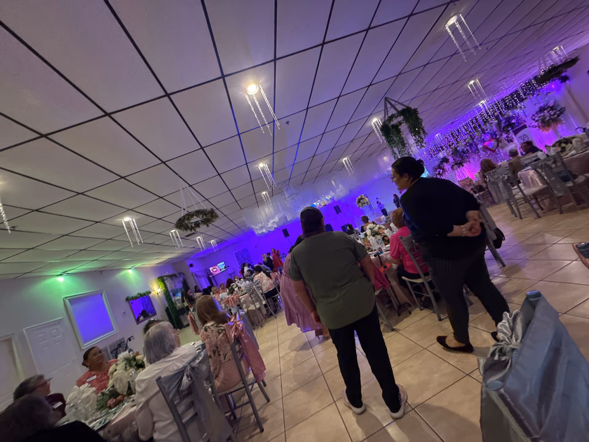A large indoor dining hall with round tables, guests seated, and purple lighting.