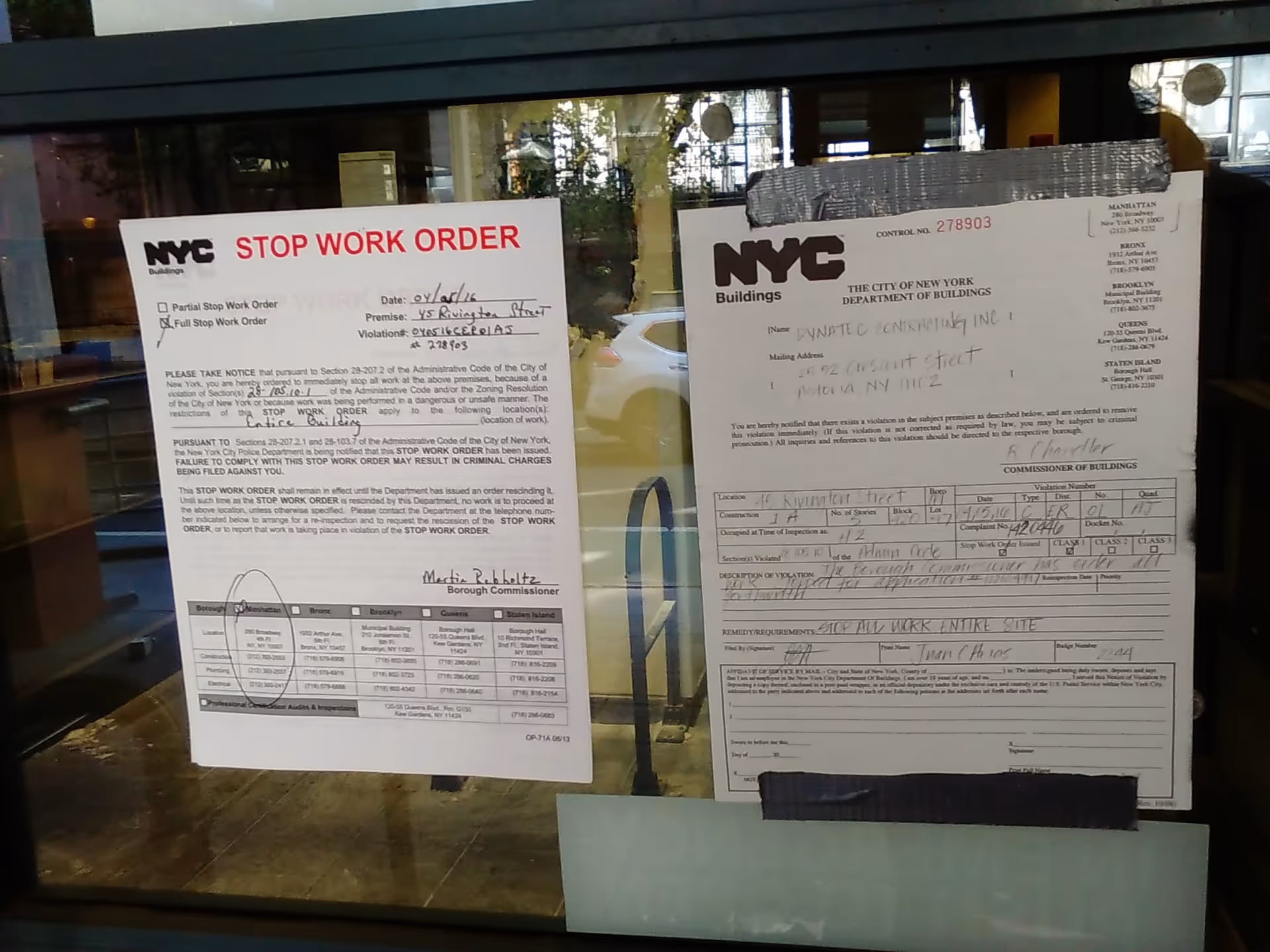 Two NYC stop-work order notices posted on a glass storefront window.