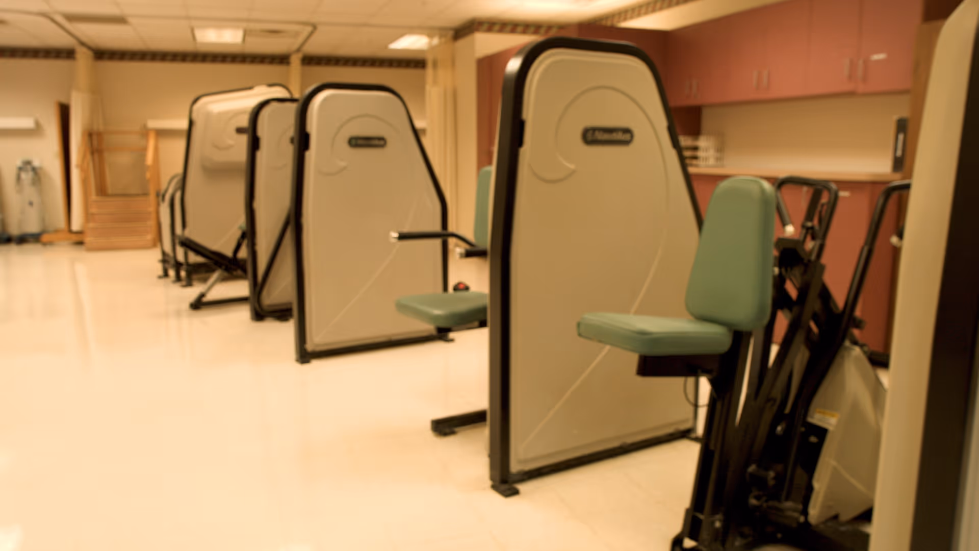 Row of stationary exercise machines in a brightly lit senior living facility fitness room.