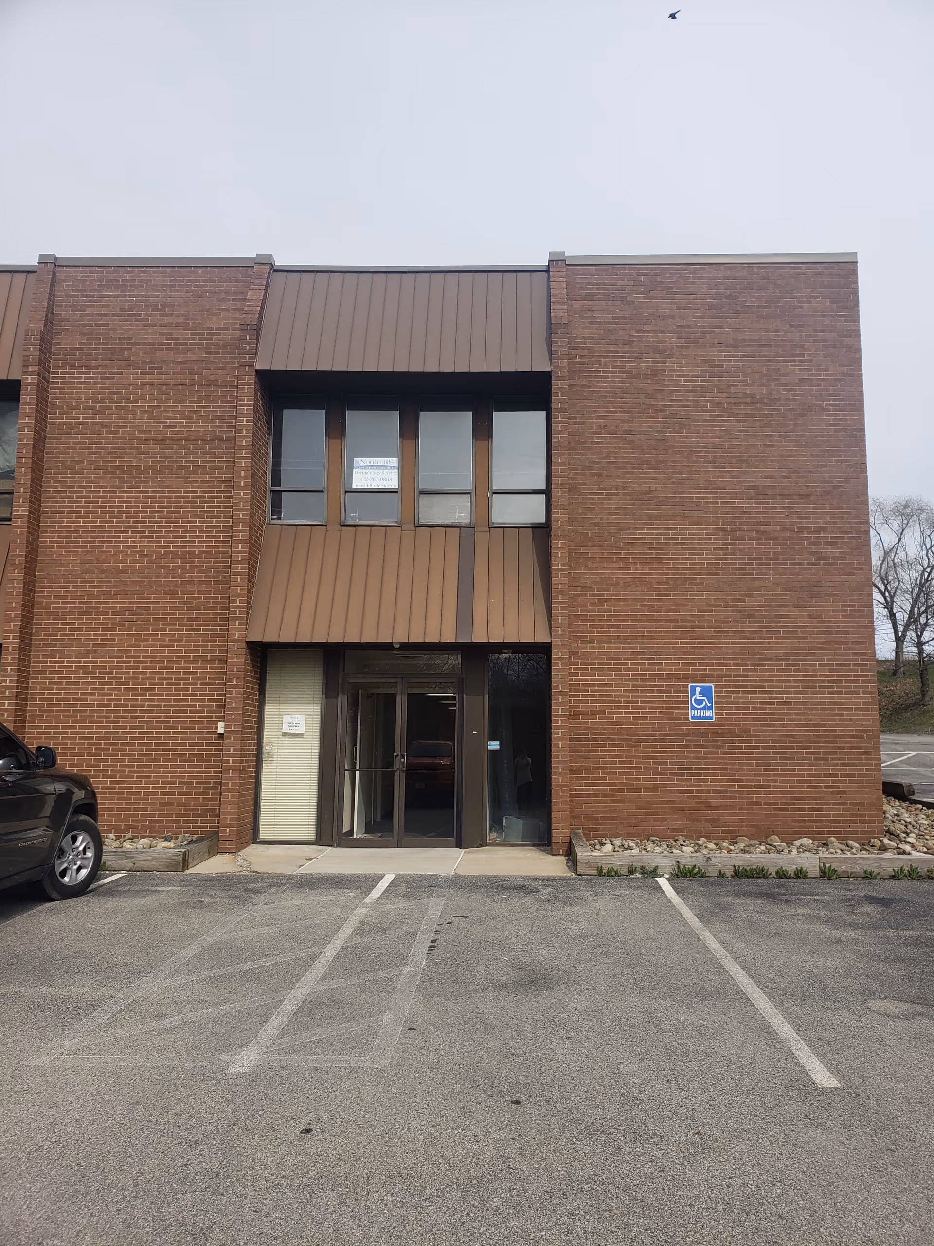 Brick facility building with glass entrance and a handicap parking sign.