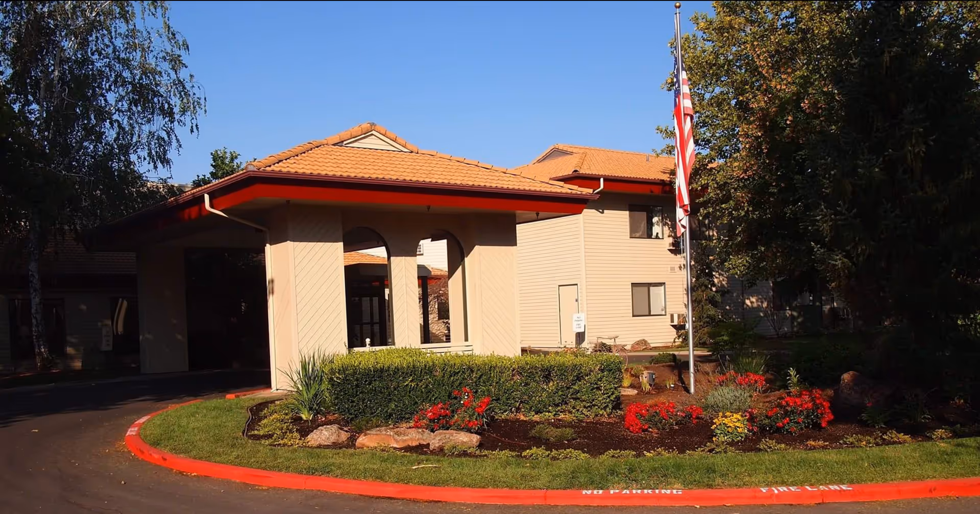 Arbor Village at Hillcrest building exterior with manicured landscaping and American flag at entrance