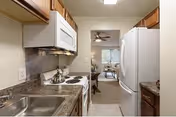 Compact kitchen with wooden cabinets, sink, stove, microwave, and refrigerator.