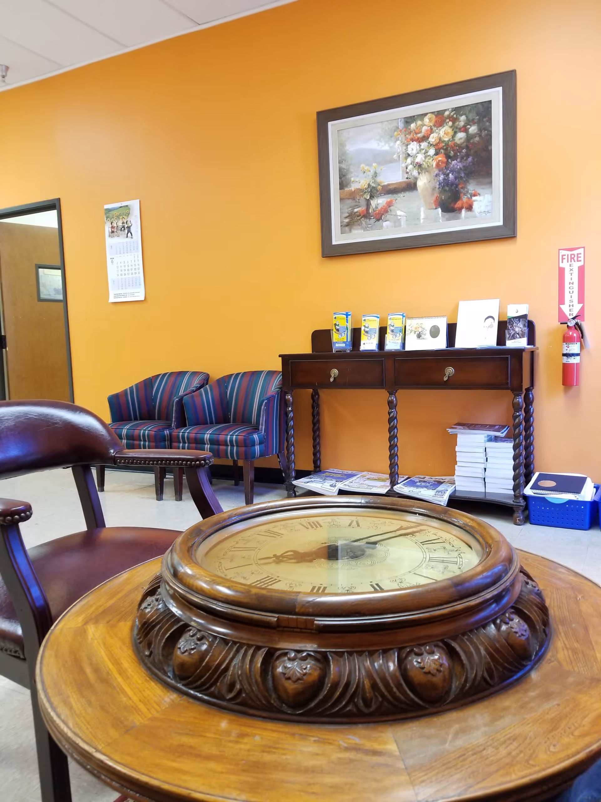 Orange-walled lounge with ornate wooden clock table and magazines on a console.