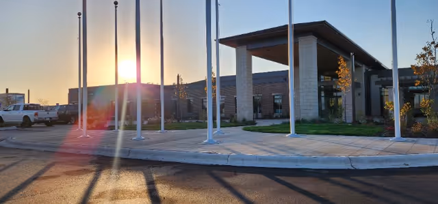 Front exterior of Minnesota Veterans Home with entrance, flags, and sun glare.