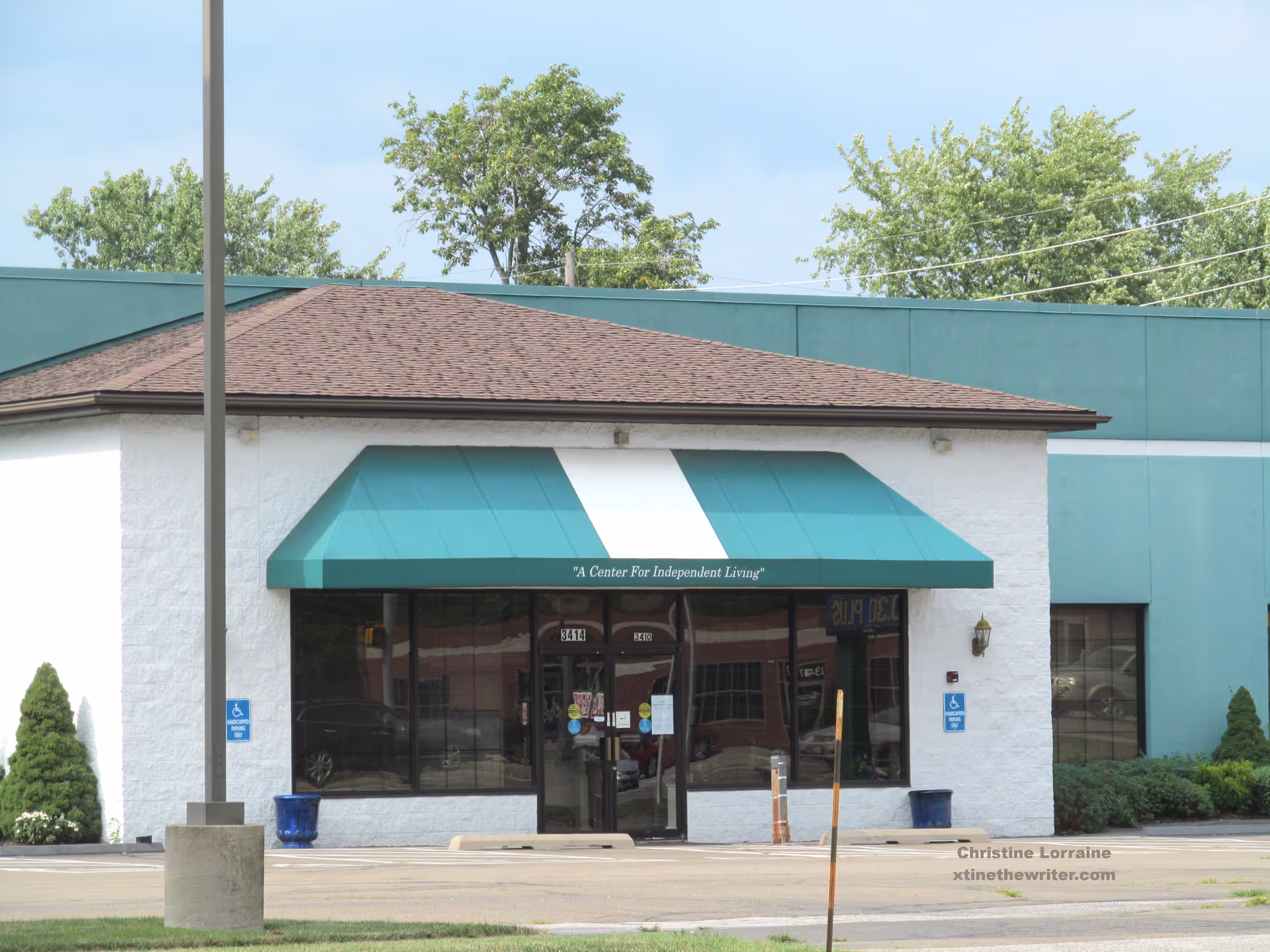 Front of a white building with a teal canopy and glass entry doors.