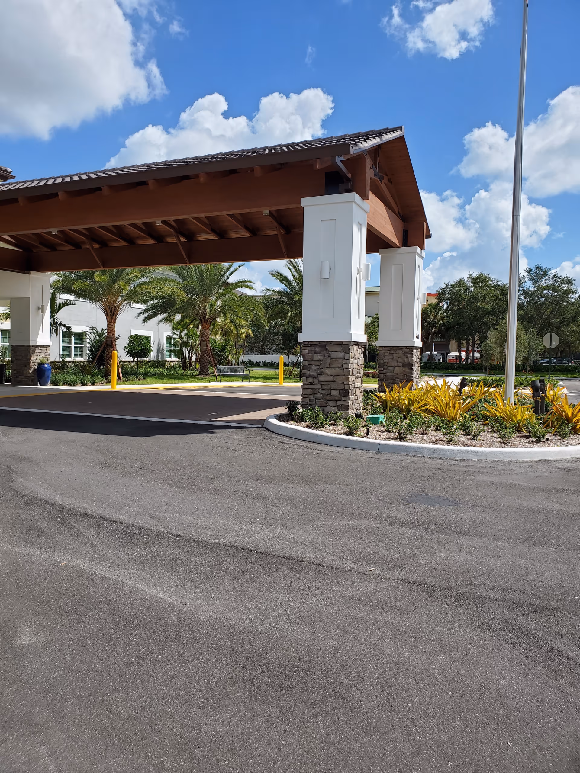 Exterior entrance of YOURLife Coconut Creek featuring a stone pillar canopy and landscaped surroundings.