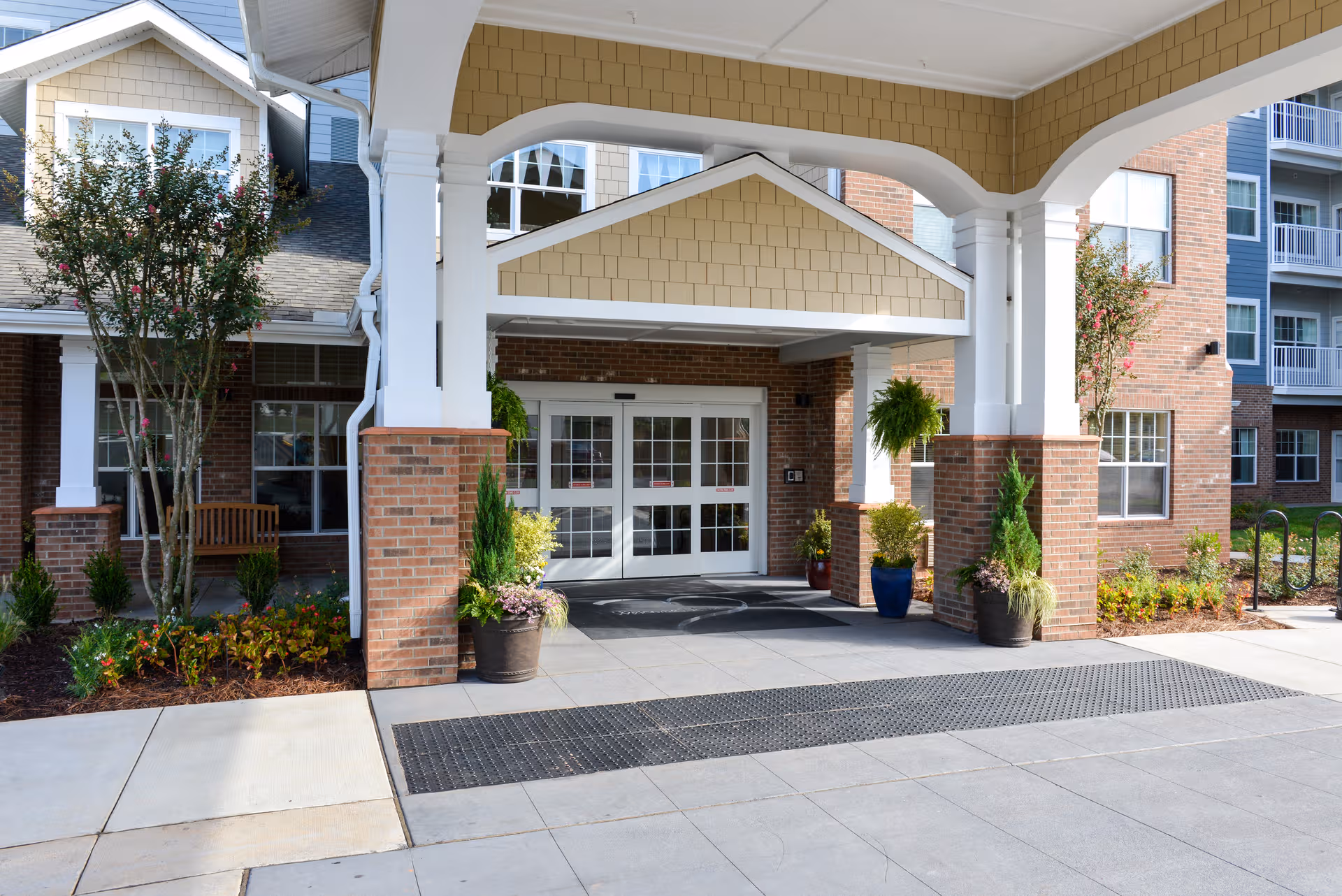 Exterior view of a senior living facility entrance with brick columns and planters.