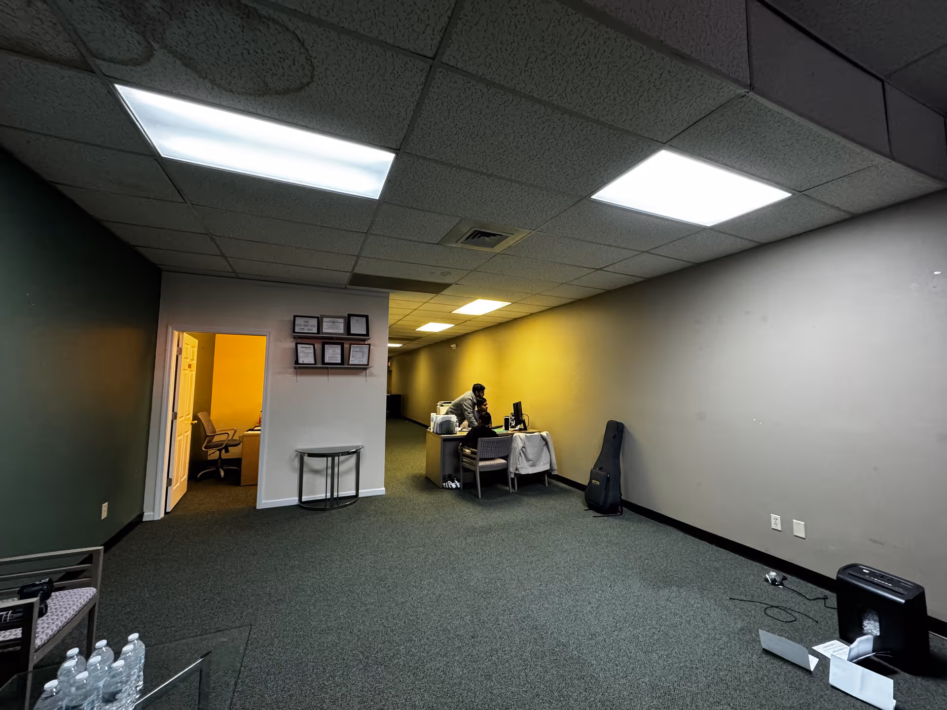 Dimly lit facility corridor with a desk, certificates on the wall, and a staff member.