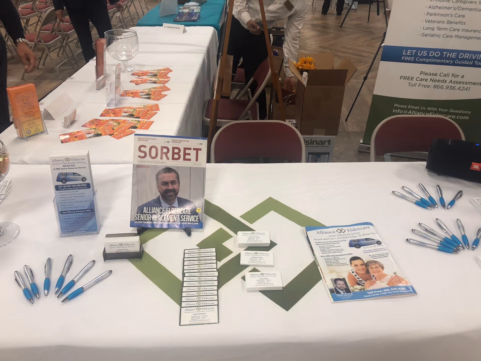 Promotional table for Alliance Eldercare with brochures, Sorbet magazine, and blue-ink pens.